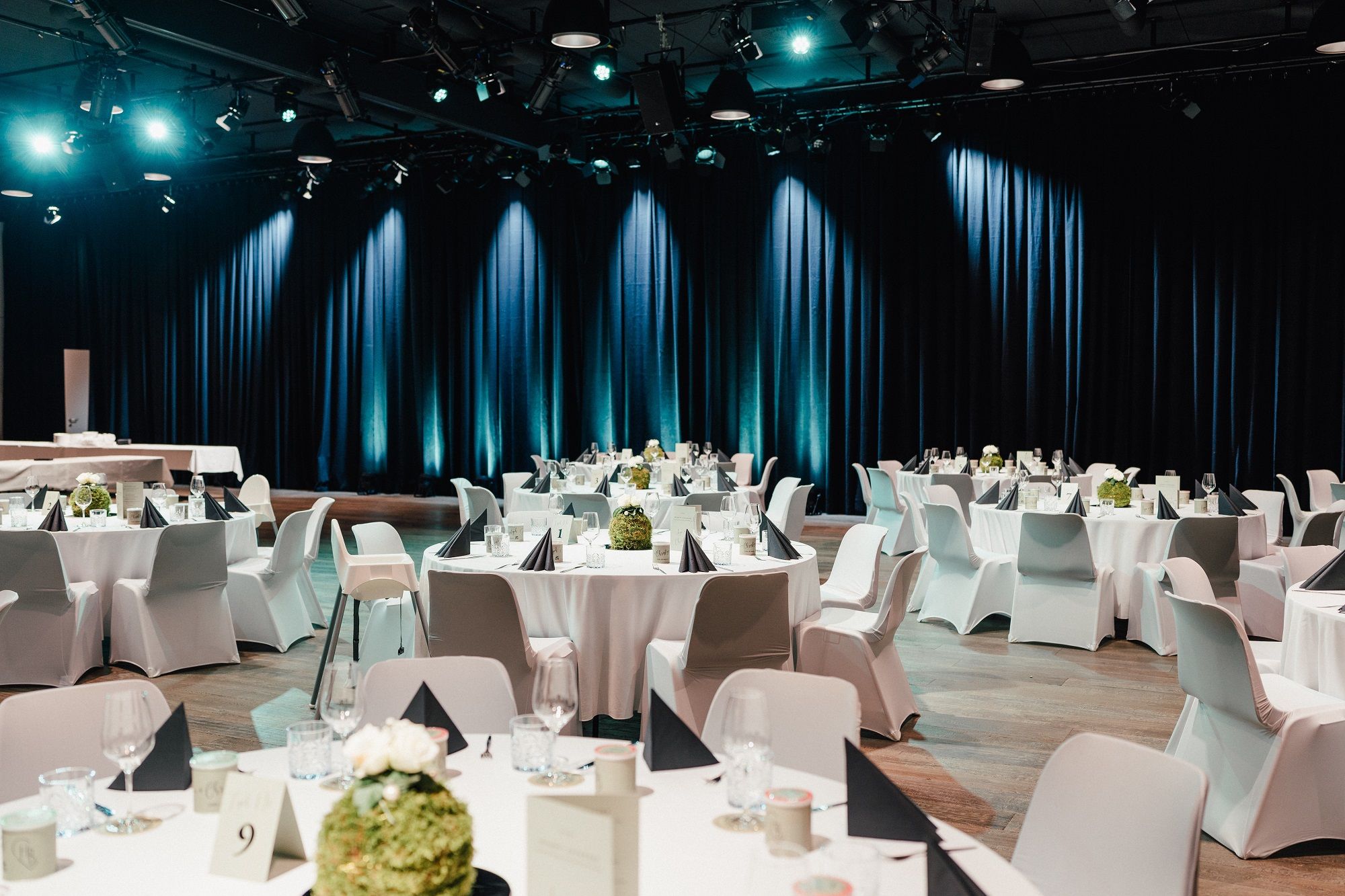 Elegant gala seating with round tables, white tablecloths and black napkins in a festively lit hall.