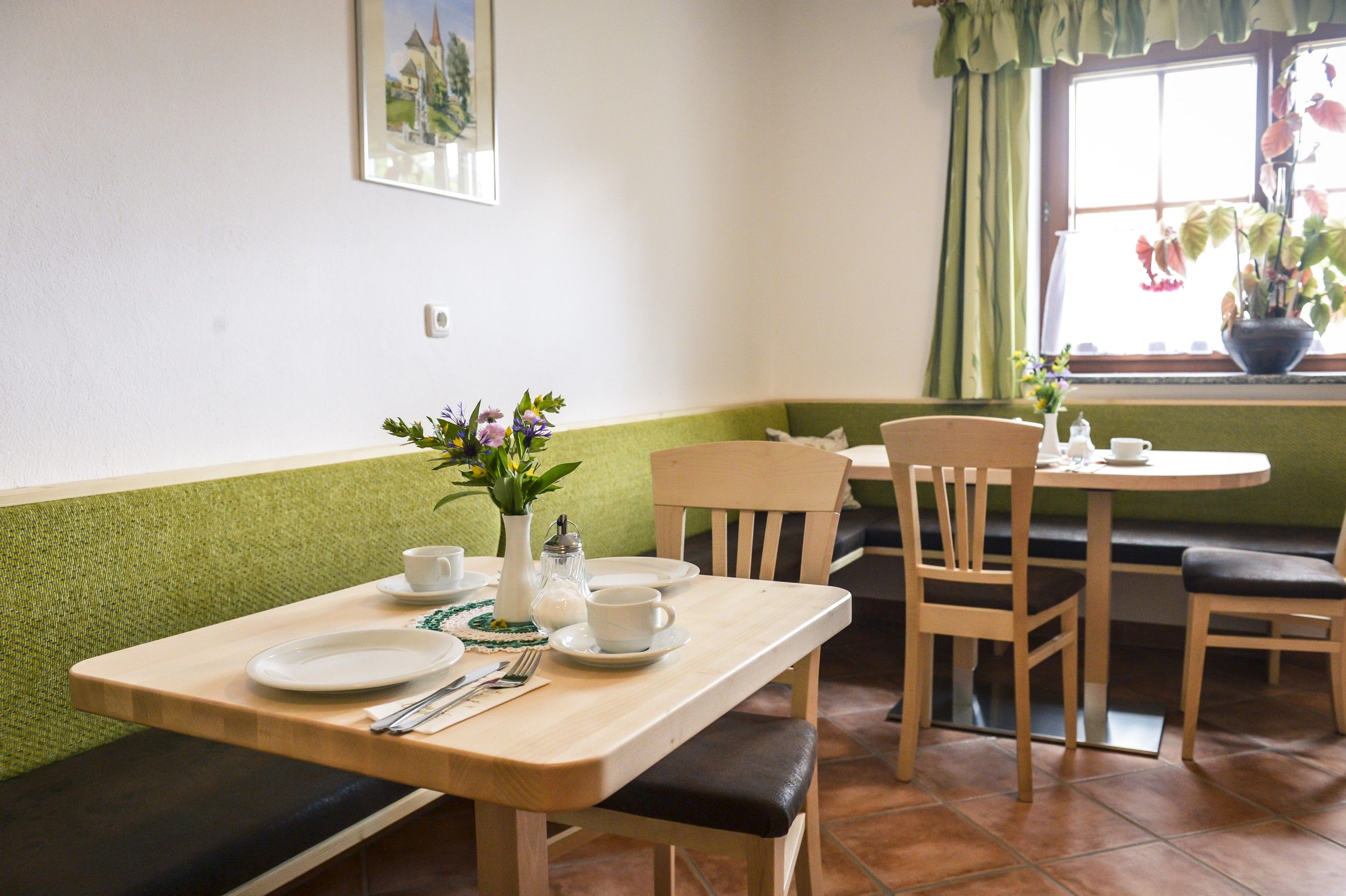 Cozy breakfast room with wooden tables, green benches and flowers on the table.