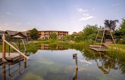 Naturhotel Molzbachhof with pond and deckchairs in the foreground.