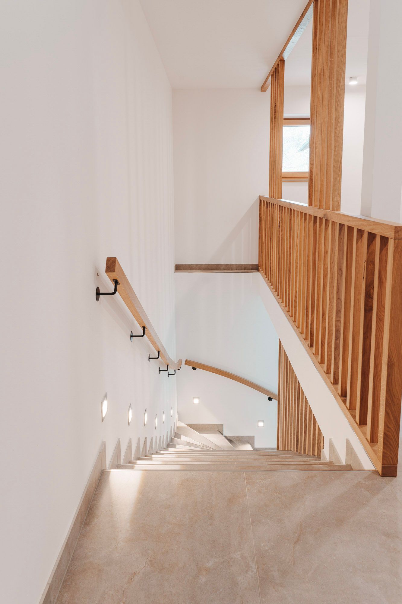 Modern staircase with wooden banisters and wall lighting in a bright interior.