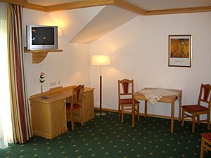 Hotel room with green carpet, wooden furniture, table, chairs and TV.