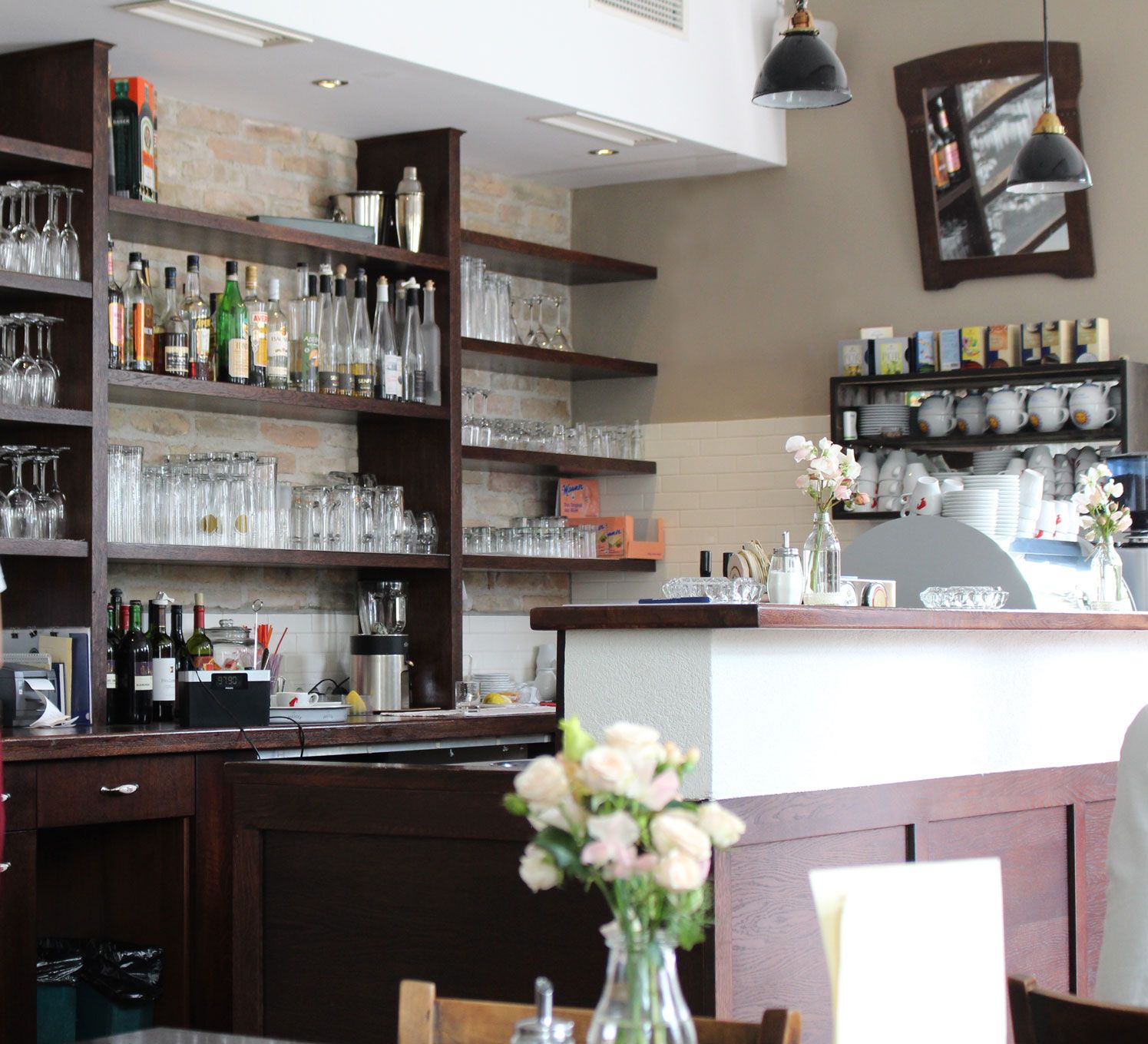 Interior view of a bar with shelves full of glasses and bottles, flowers on the counter.