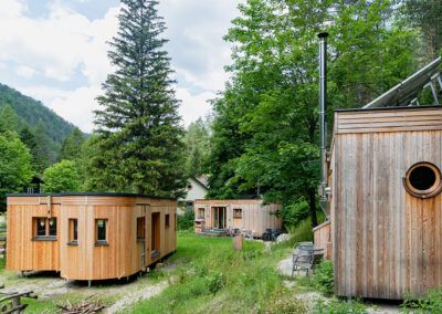 Three small wooden houses in a green forest landscape.