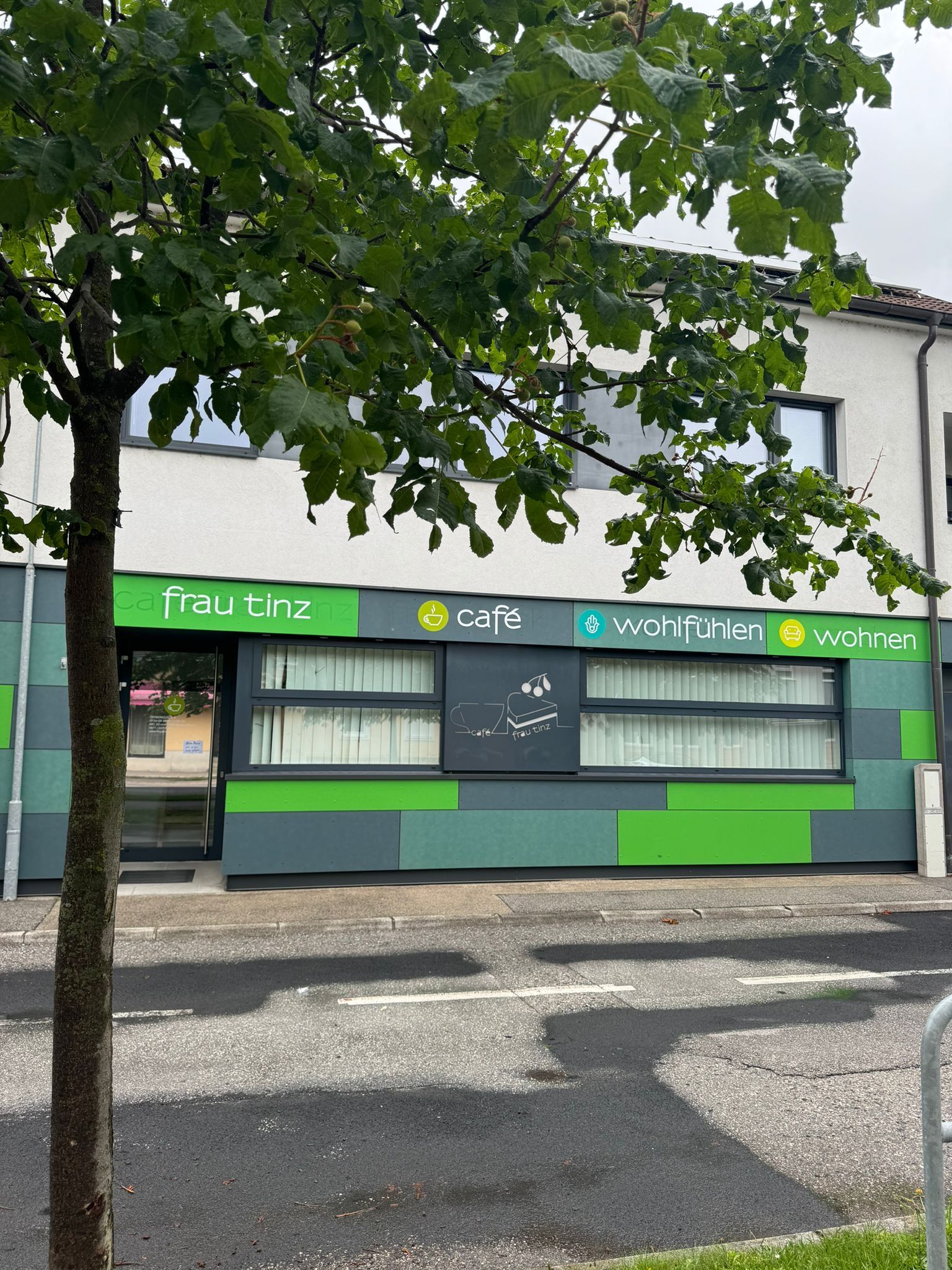 Exterior view of a café with green façade and tree in the foreground.