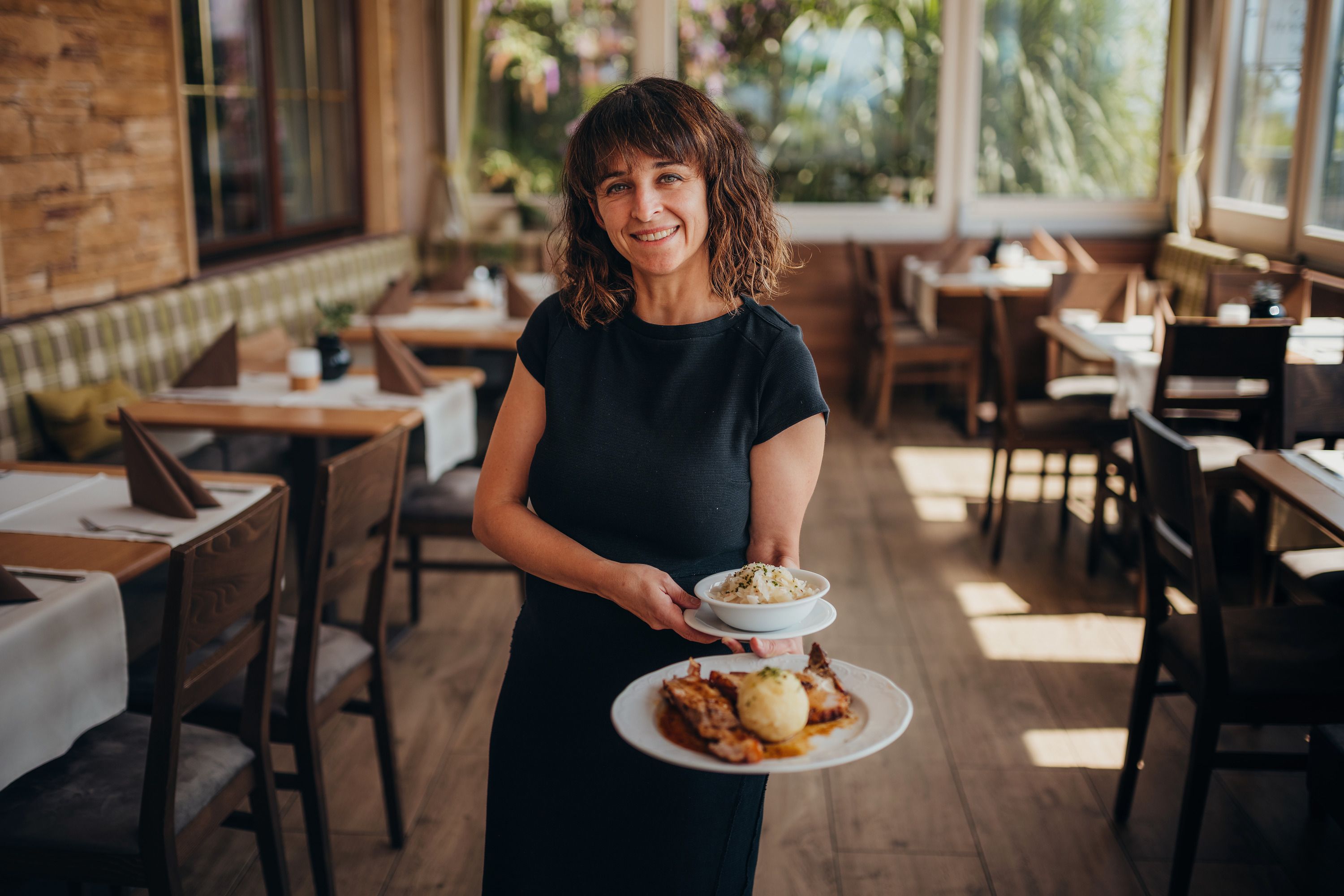 Woman serves food in a cozy restaurant with wooden furniture.
