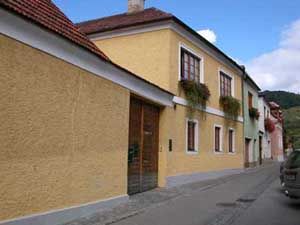 Yellow house with red roof tiles and flower boxes on the windows in a narrow street.