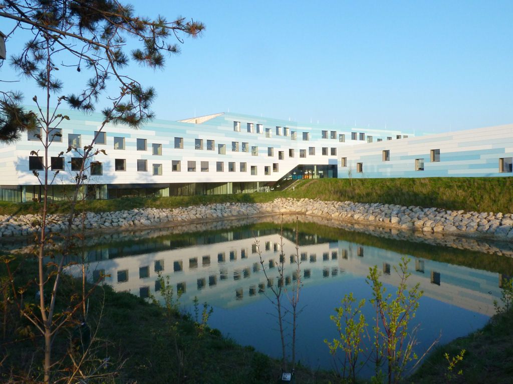 Modern building with blue and white façade and pond in the foreground.
