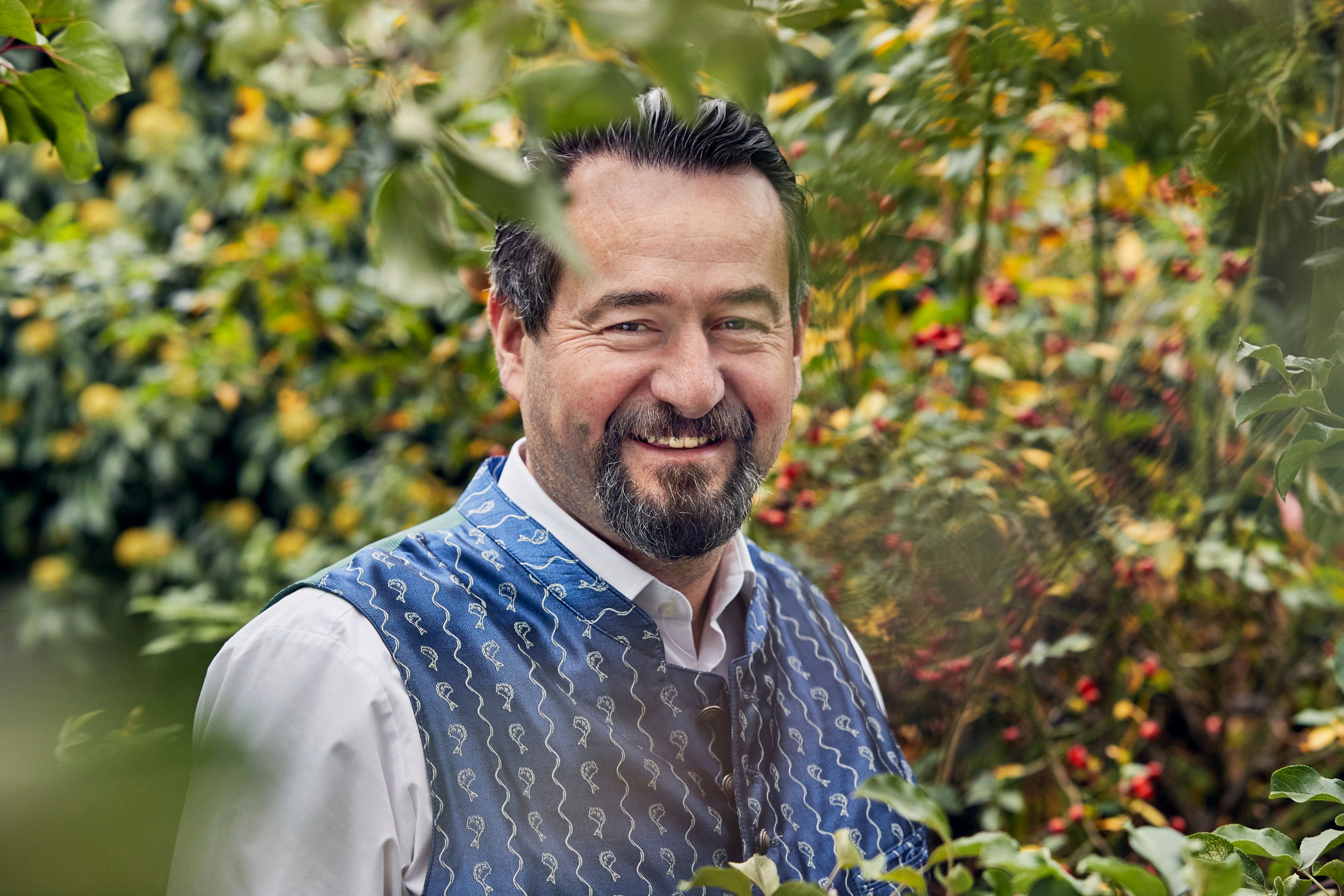 A man in traditional dress smiles in a garden.