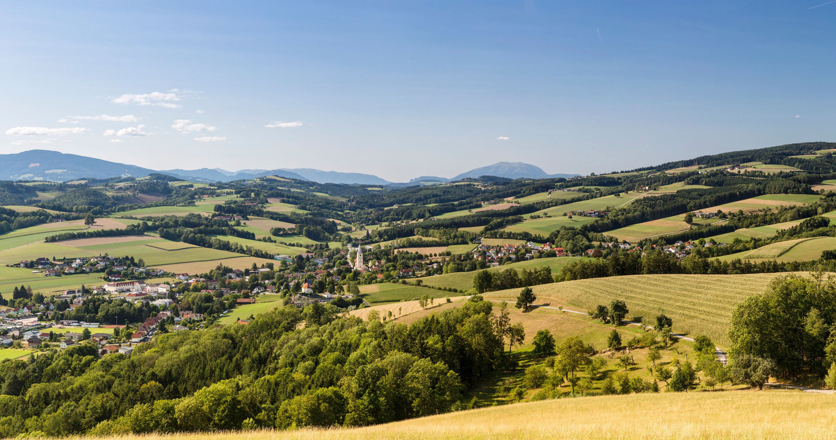 Panoramic view of the Bucklige Welt region, showing the town of Krumbach with its church tower in the valley, with hills and the Schneeberg mountain in the background.