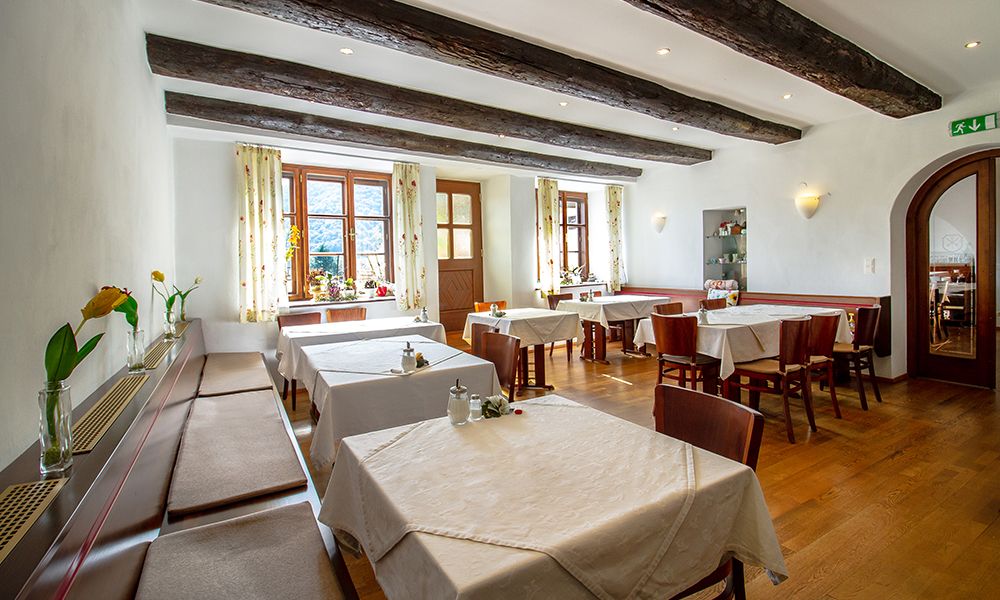 A cozy breakfast room with wooden beams, laid tables and flowers on the windowsills.