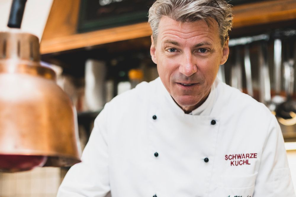 Cook in white uniform in a kitchen with copper lamp.