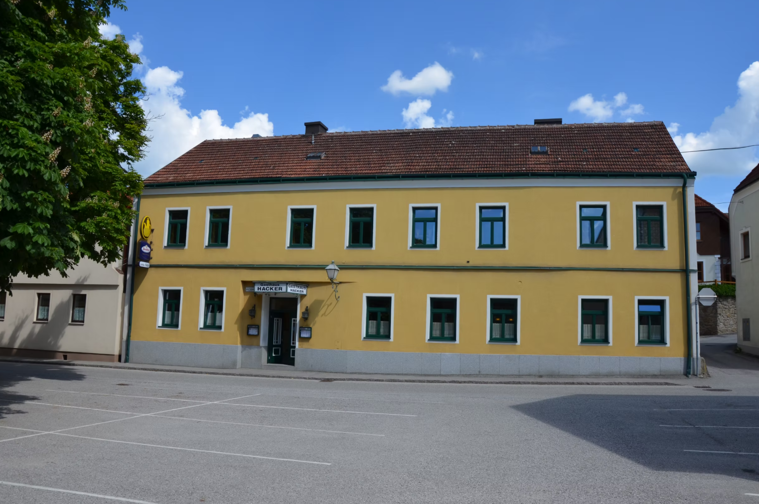 Yellow two-story building with green window frames and a sign with the inscription 'Gasthaus Georg Hacker'.