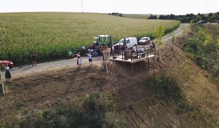 Aerial view of a viewpoint with people, vehicles and a field in the background.