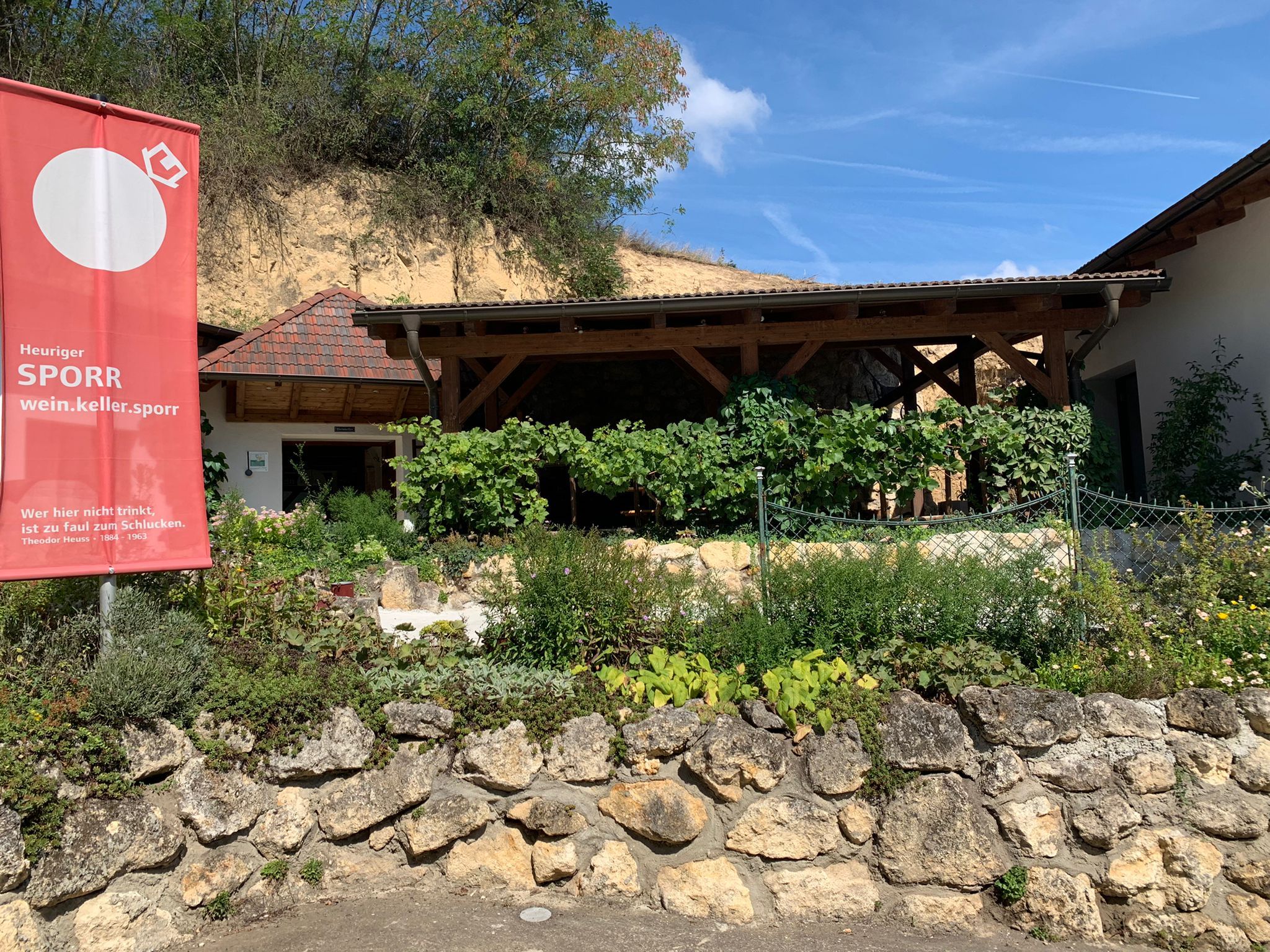 Exterior view of a wine tavern with garden and advertising sign.