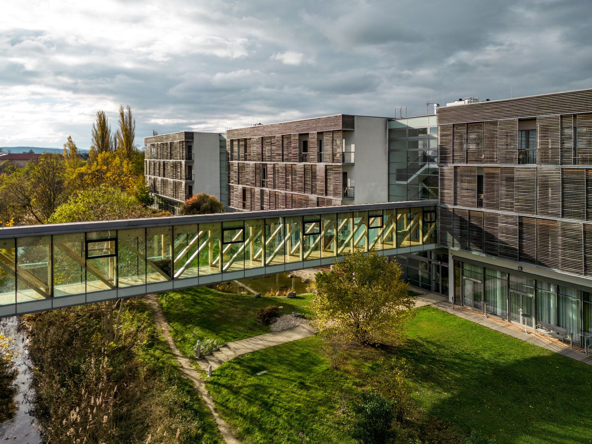 Modern hotel building with glass bridge and garden.