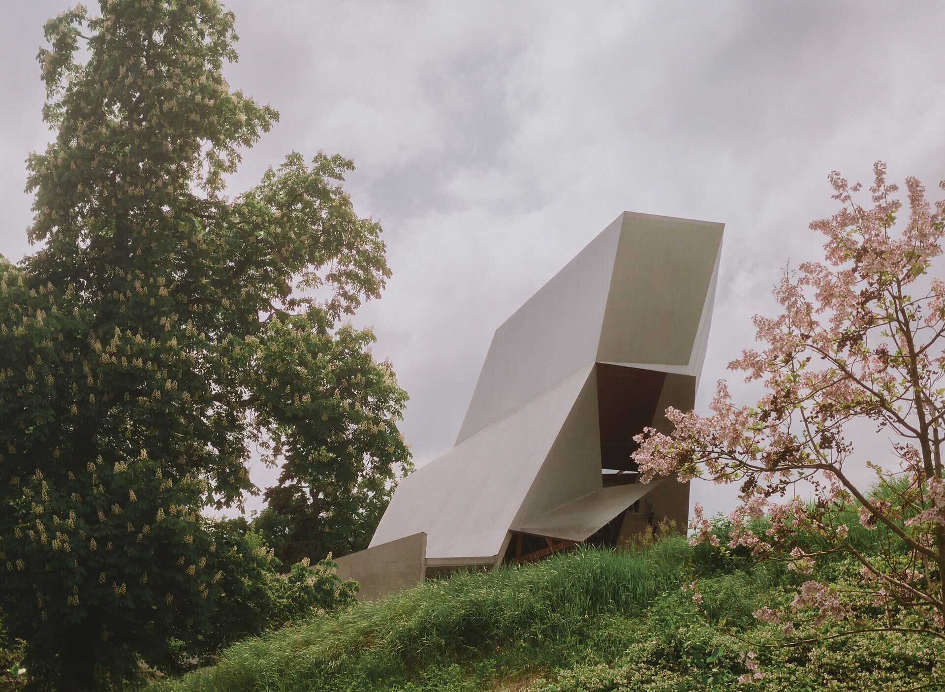 Der Wolkenturm in Grafenegg – moderne Freiluftbühne aus Beton und Stahl, umgeben von blühenden Bäumen und grüner Landschaft unter einem leicht bewölkten Himmel.