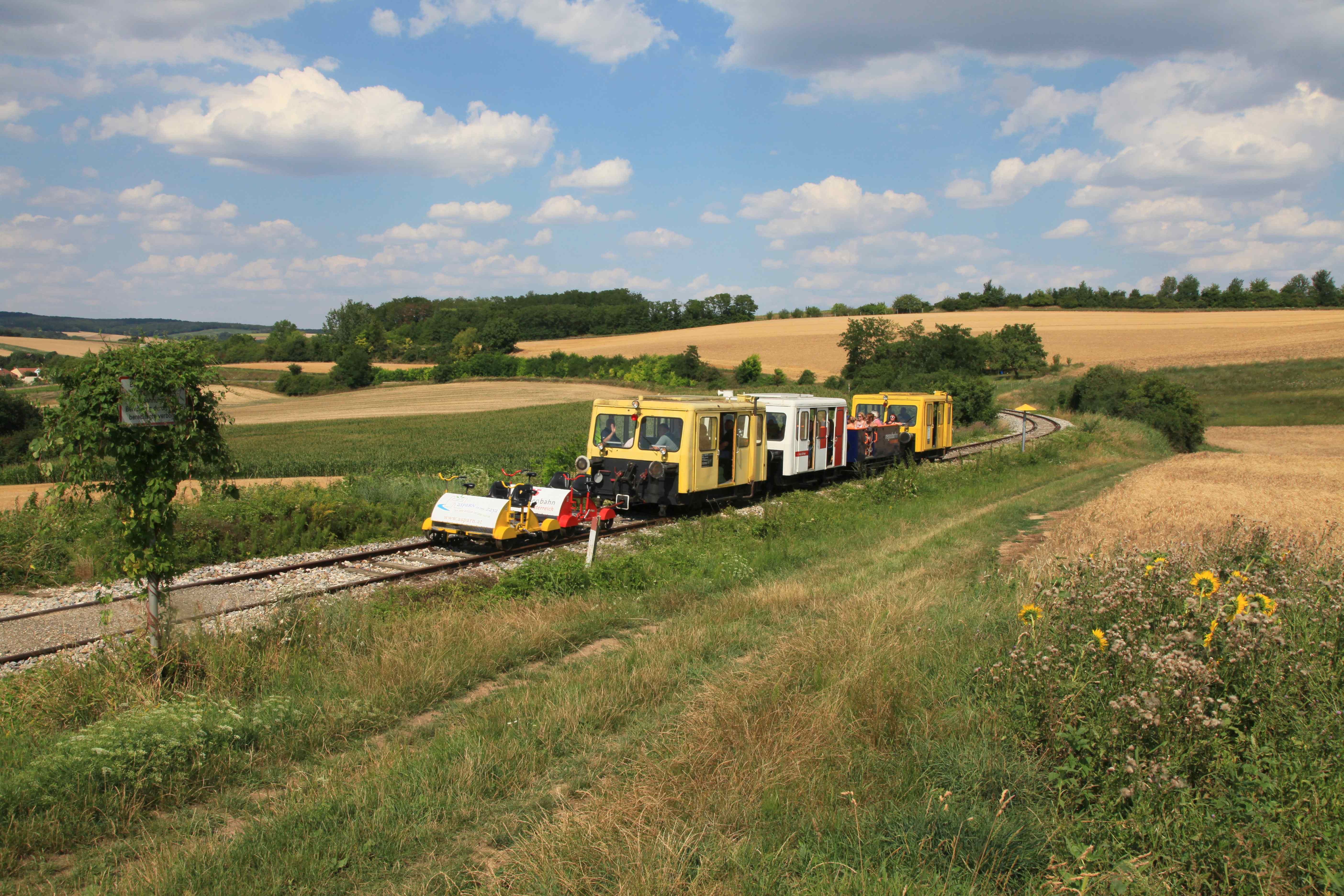 Draisines on a rural railroad line in a hilly landscape with fields and trees.