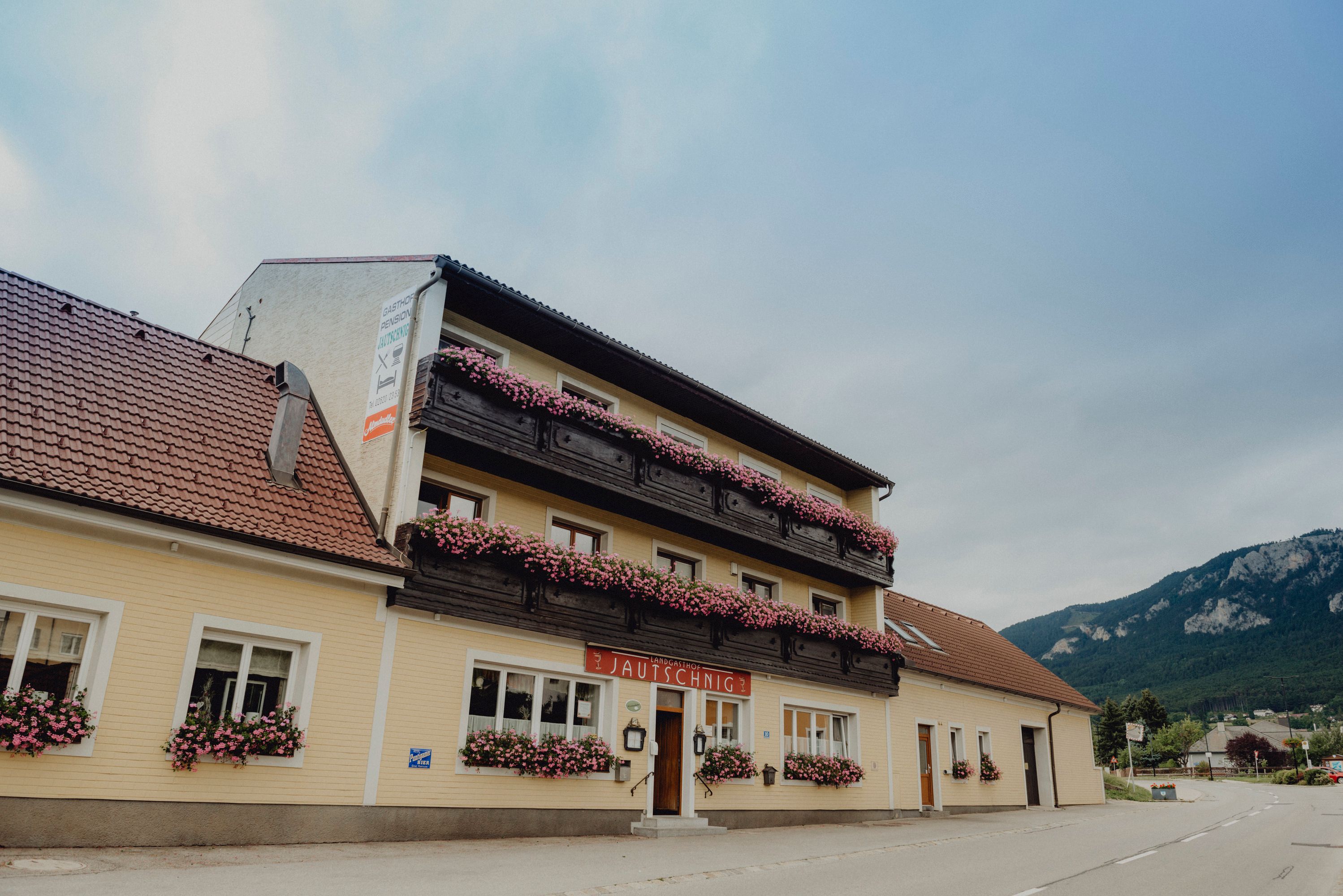 A traditional country inn with balconies decorated with flowers against a mountain backdrop.