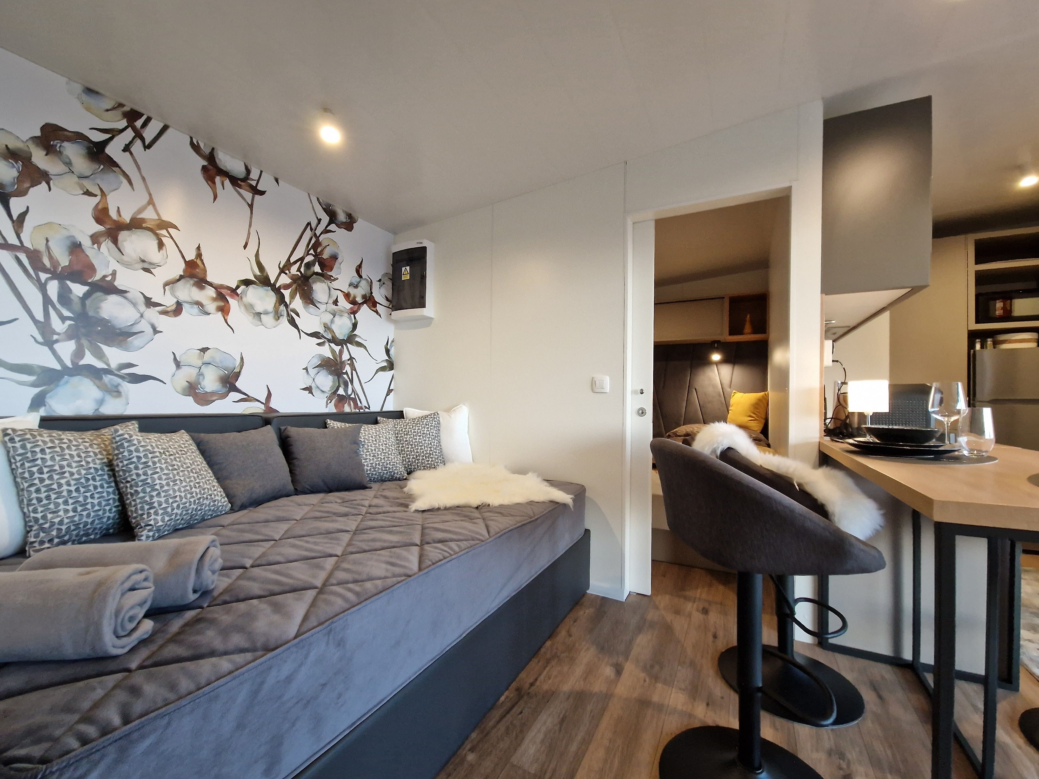 Interior view of a modern chalet with gray sofa, decorative flower wall, bar stool and dining table.