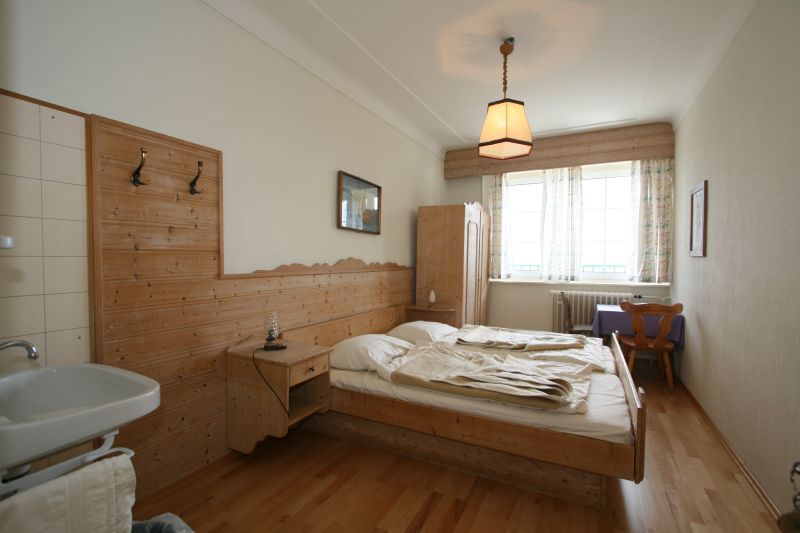 Comfortable hotel room with wooden furniture, double bed, washbasin and window with curtains.