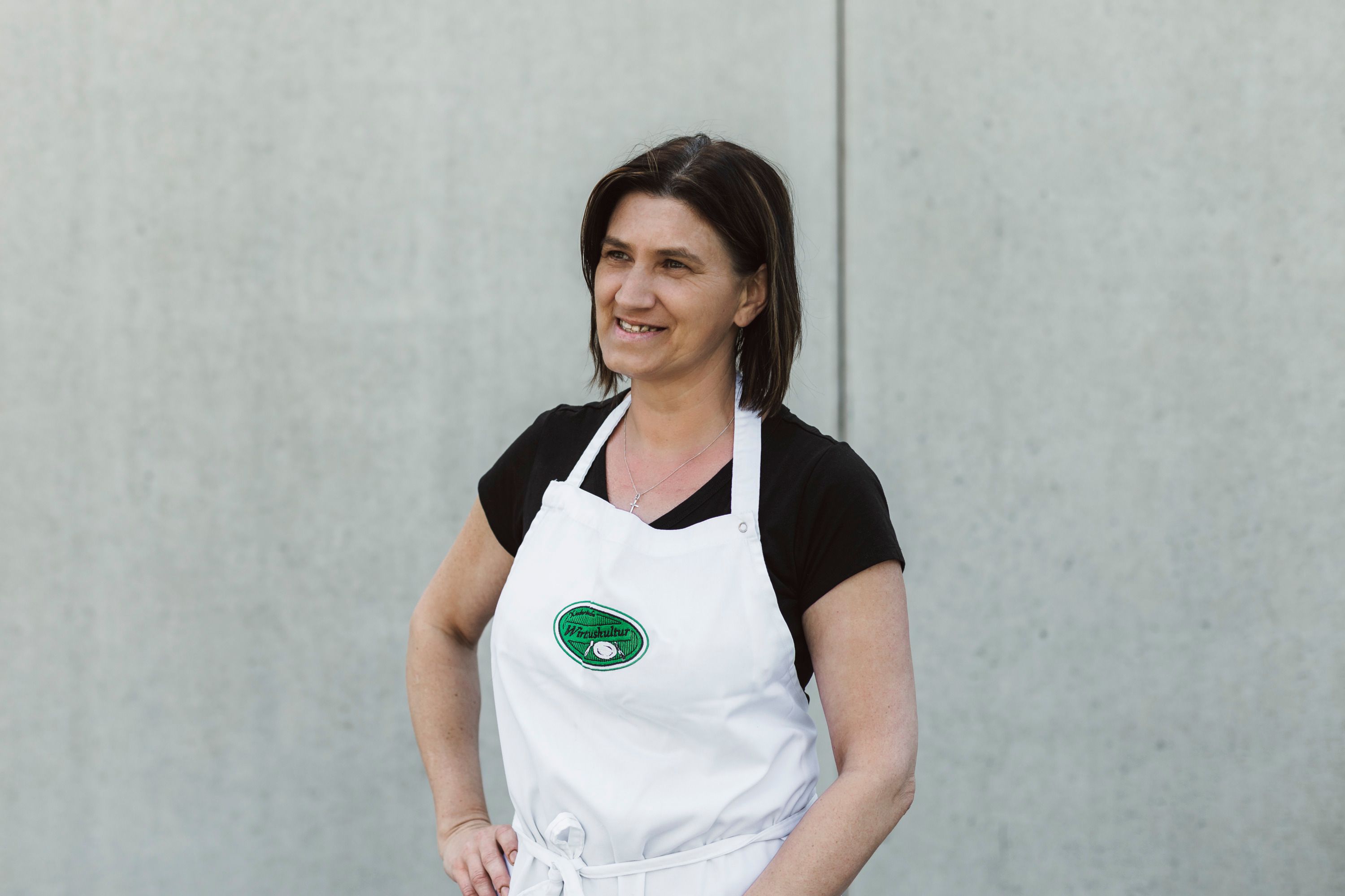 Woman in a white apron in front of a gray wall.