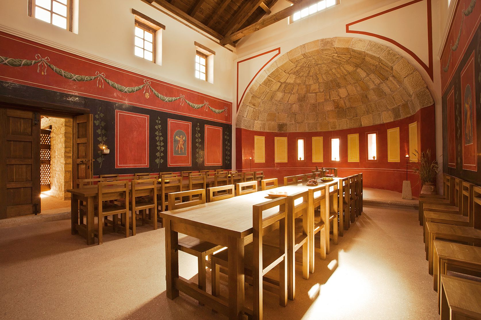 Interior view of a Roman dining room with wooden tables and chairs, red walls and decorative frescoes.