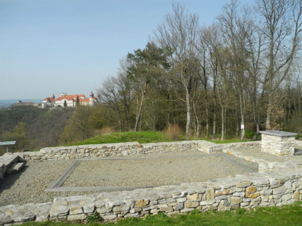 Ruins of an old stone wall with a castle in the background on a hill.