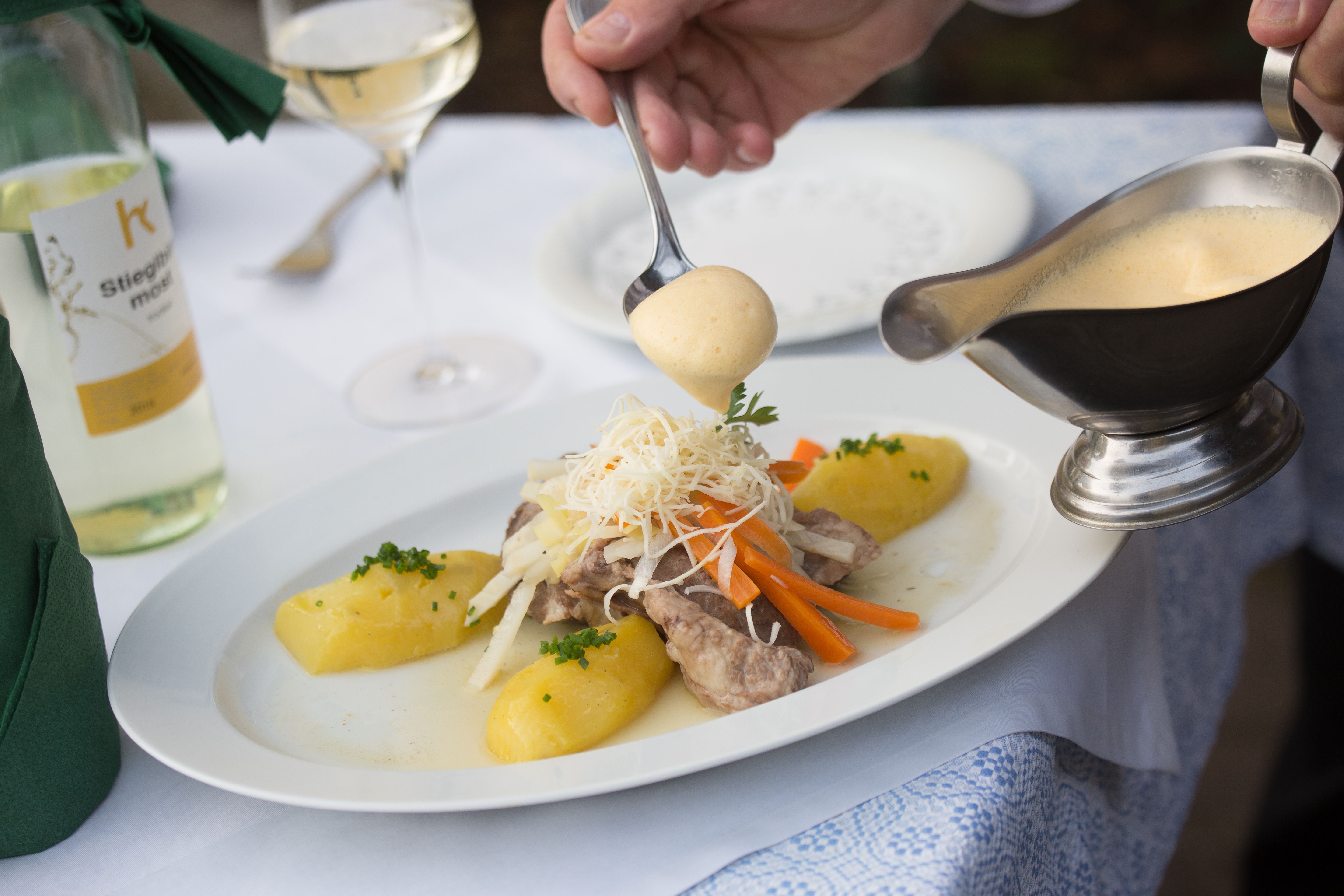 A plate of meat, vegetables and potatoes is poured over with sauce.
