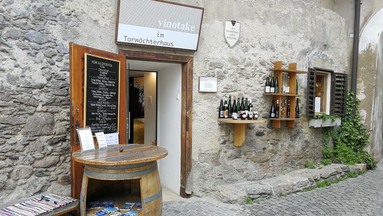 Entrance to a wine store in an old stone building with wine barrels and bottles on the wall.