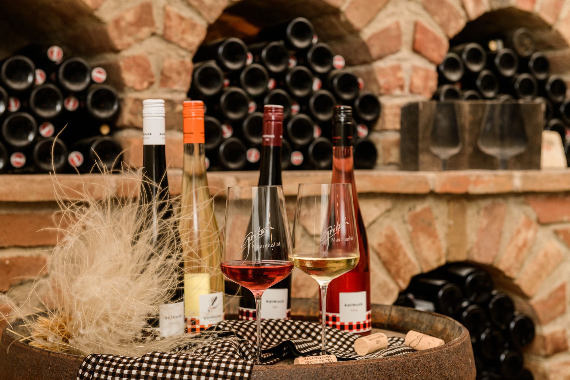 Wine bottles and glasses in front of a shelf with wine bottles in a wine cellar.