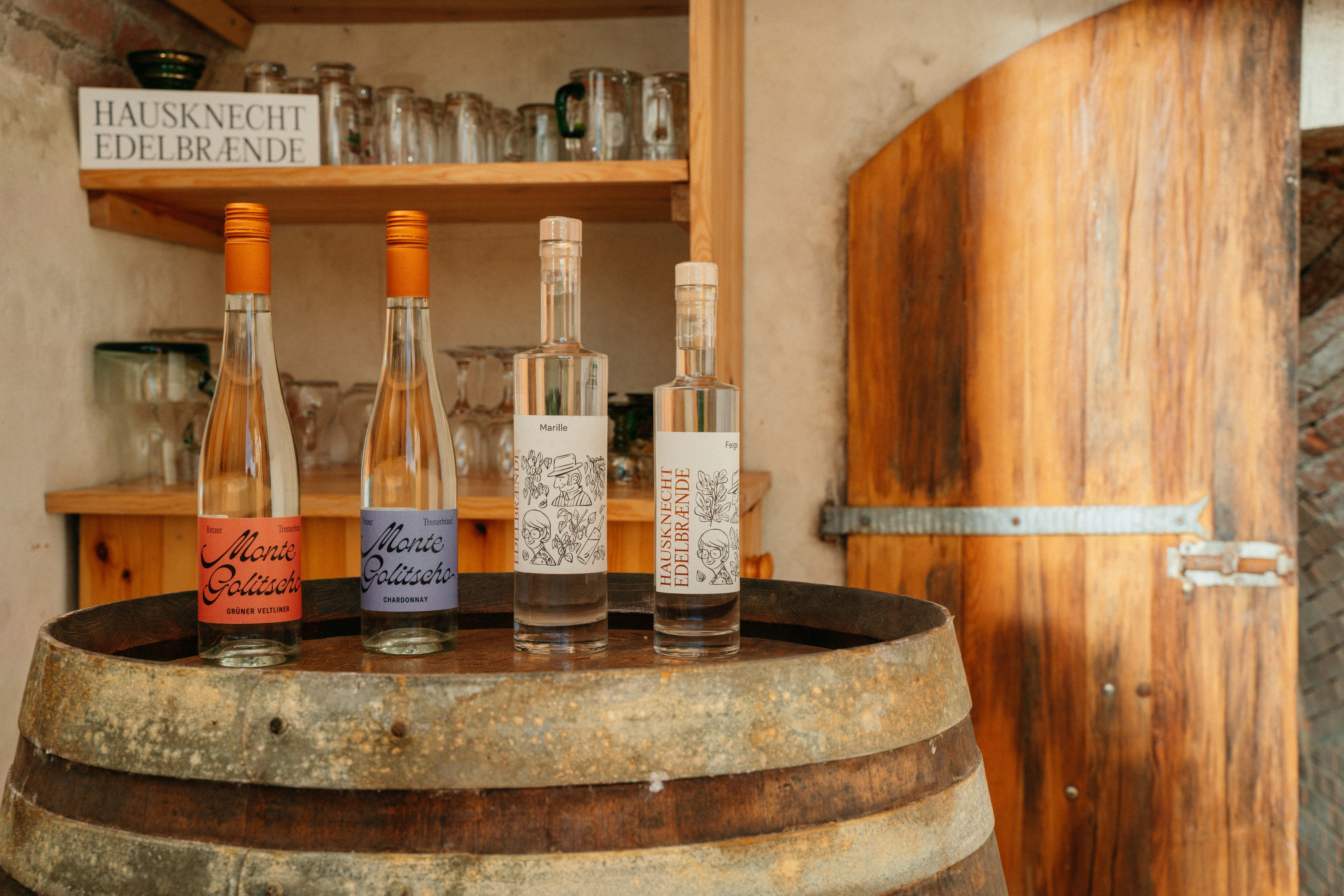 Three bottles of brandy on a wooden barrel in a rustic room.