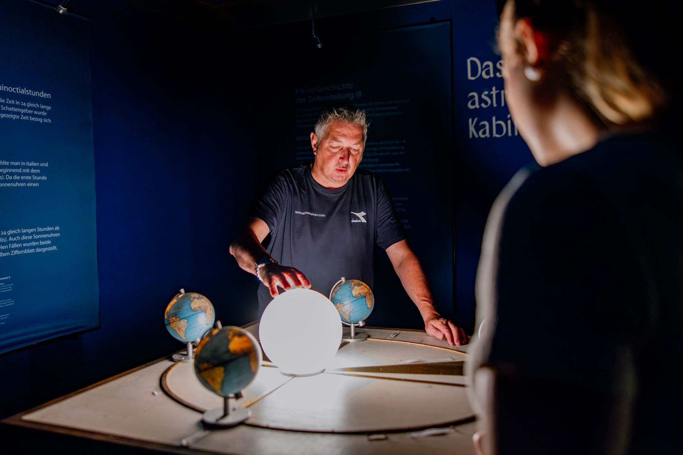 A man uses a model to explain the course of the sun in a dark room.