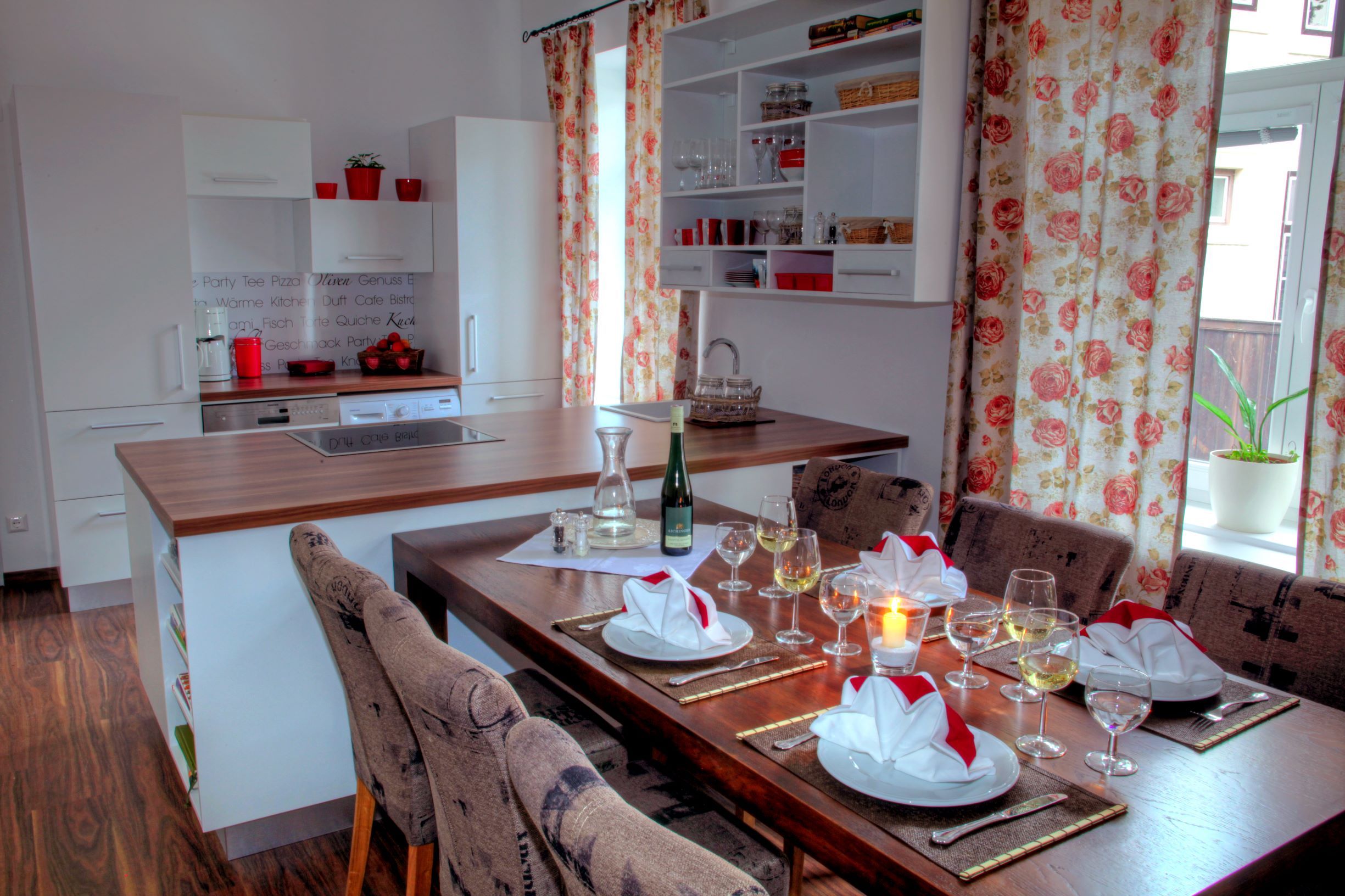 Modern kitchen with dining table, set with glasses and napkins, floral pattern curtains.
