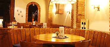 Cozy parlor with wooden table and chairs, surrounded by rustic brick arches and warm light.