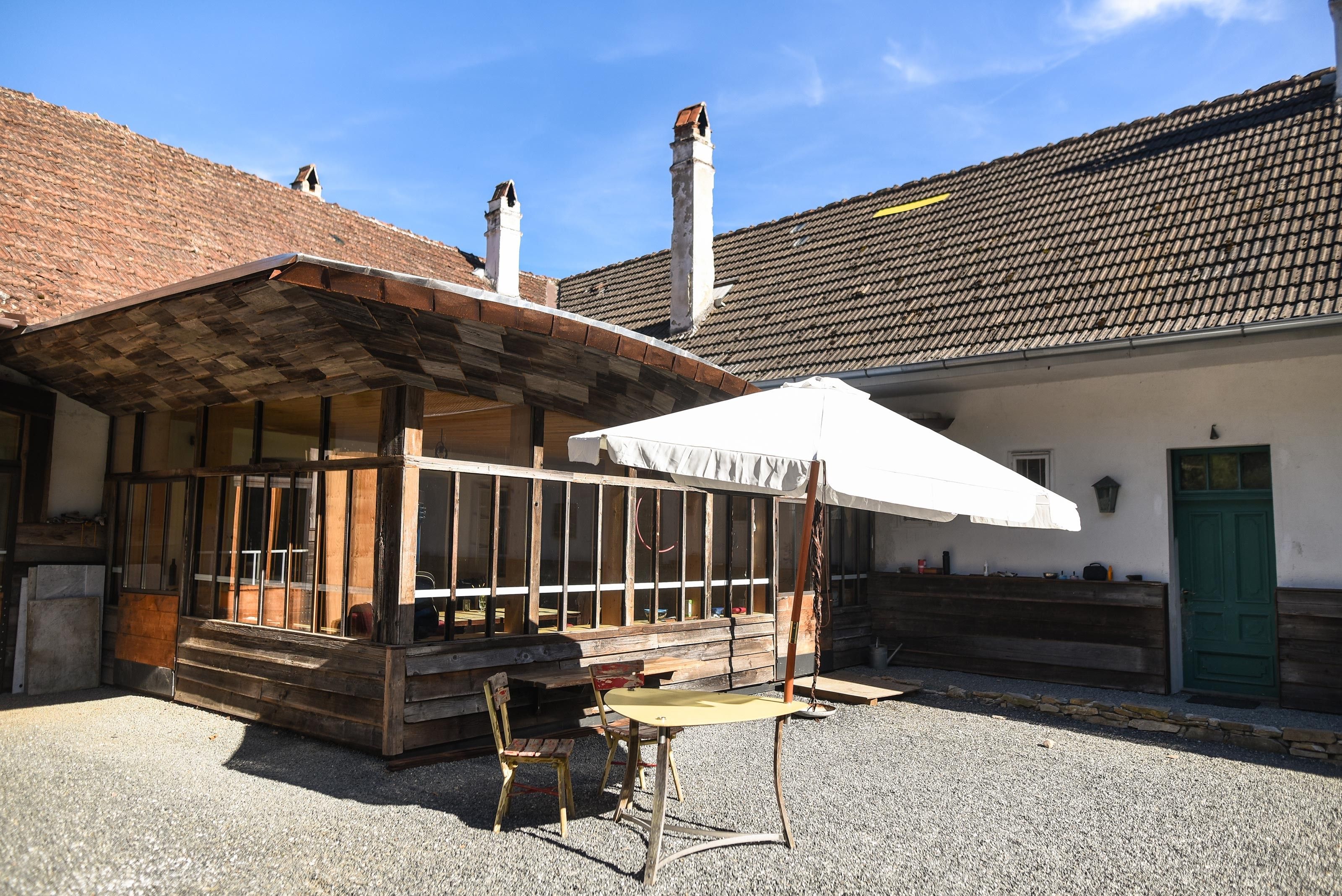A rustic courtyard with a wooden structure, a table, and chairs under a parasol.