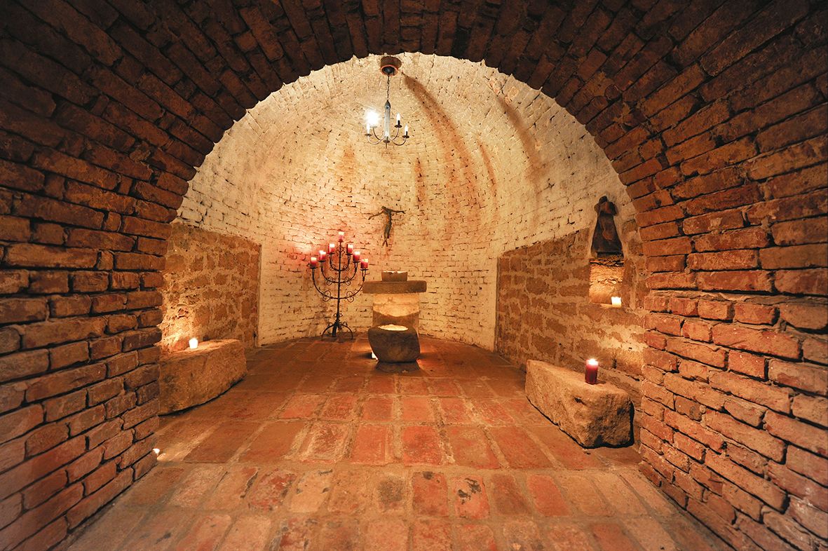 A rustic, vaulted cellar room with candles and an altar.