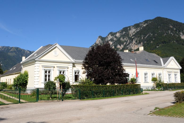 A large, bright building with a garden against a mountain backdrop.