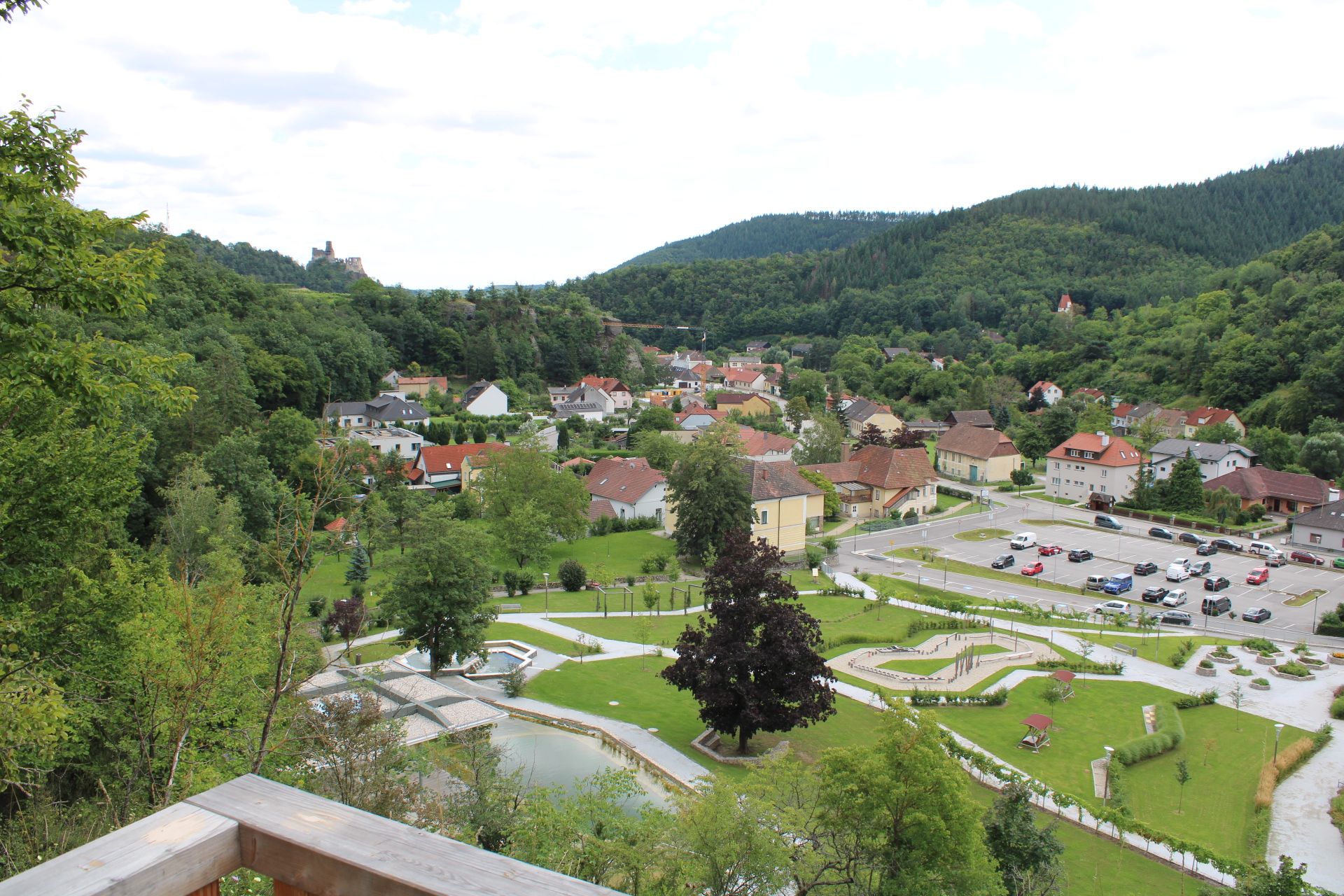 View from a viewing platform of a town with surrounding woods and a ruined castle in the background.