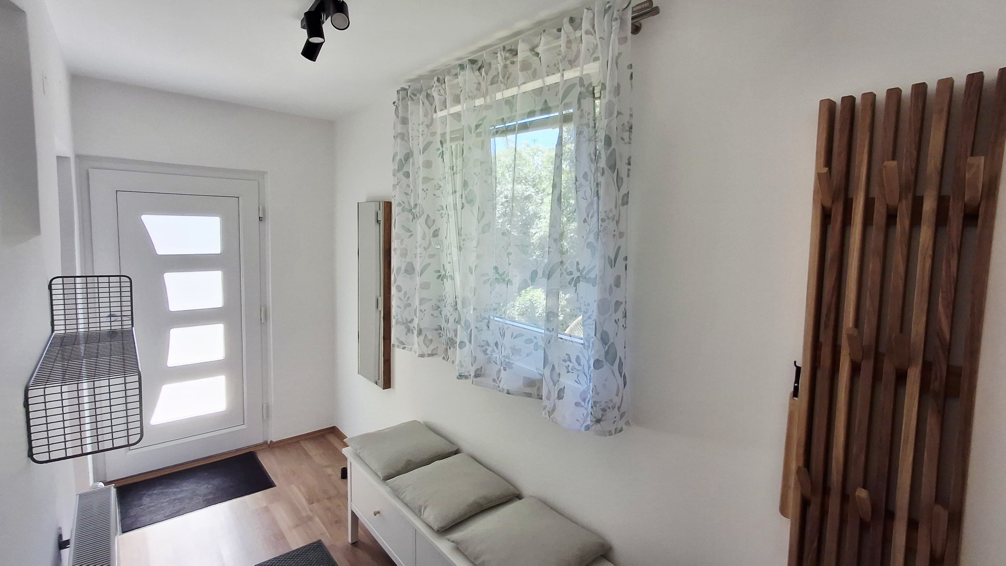Bright entrance area with white door, wooden floor, bench and coat rack.