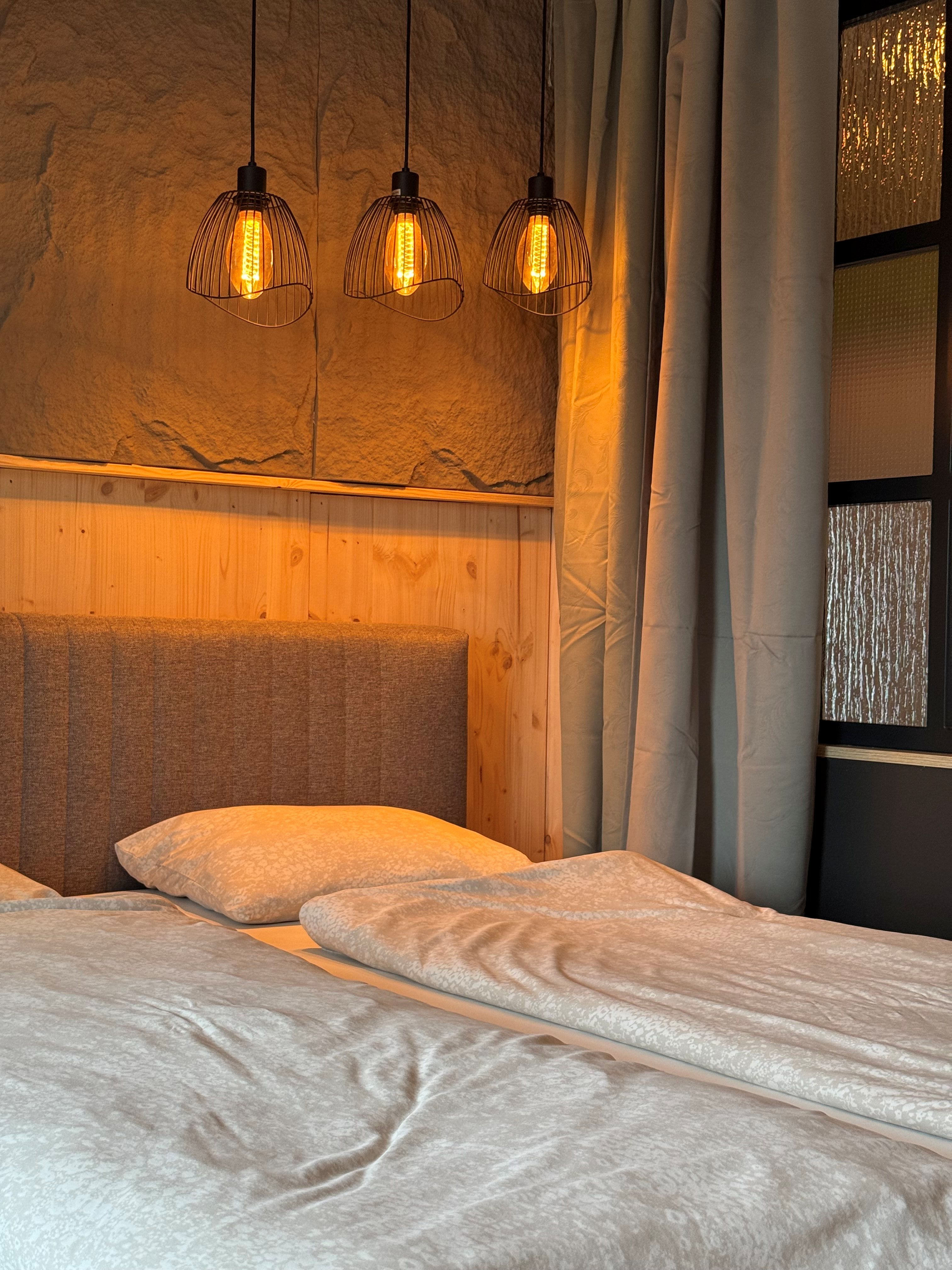 A cozy bedroom with a double bed, wood paneling, and three hanging lamps.