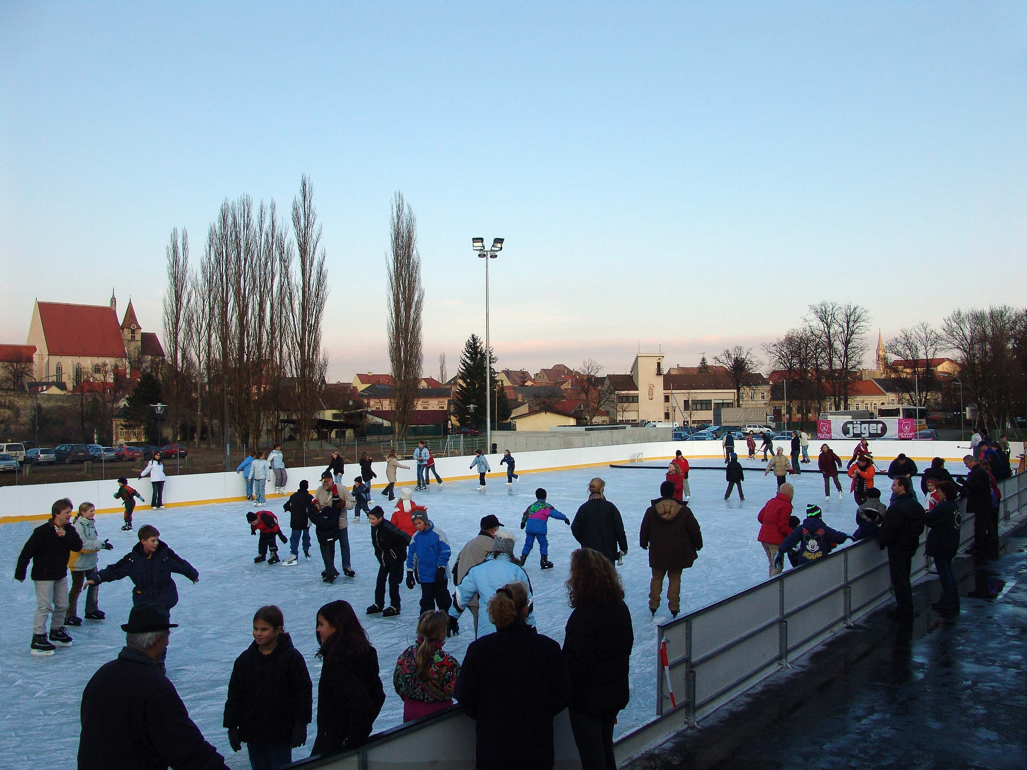 People skating on an open-air ice rink with a church in the background.