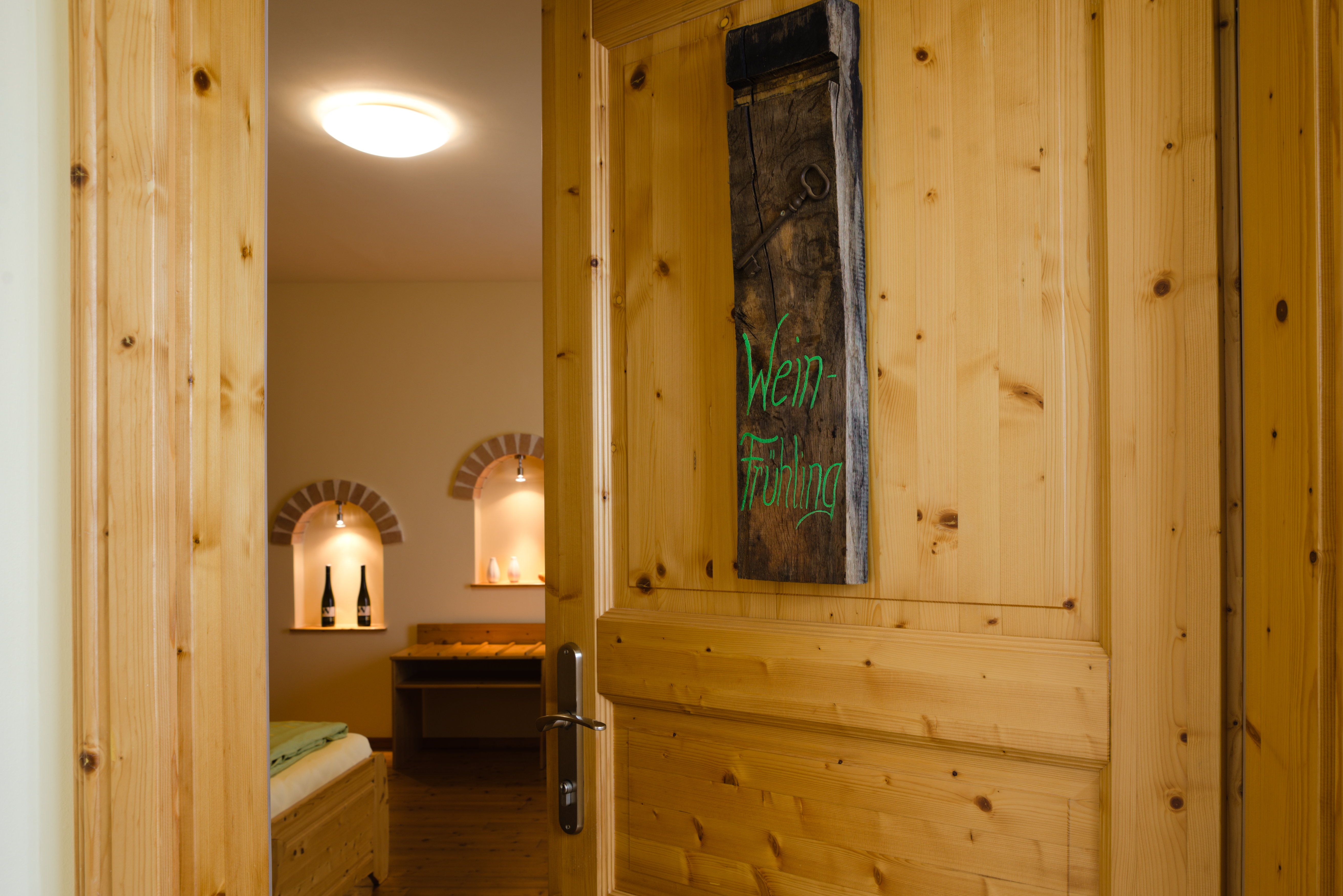 Open wooden door with sign 'Wein-Frühling', view into a cozy room with wine bottles in niches.