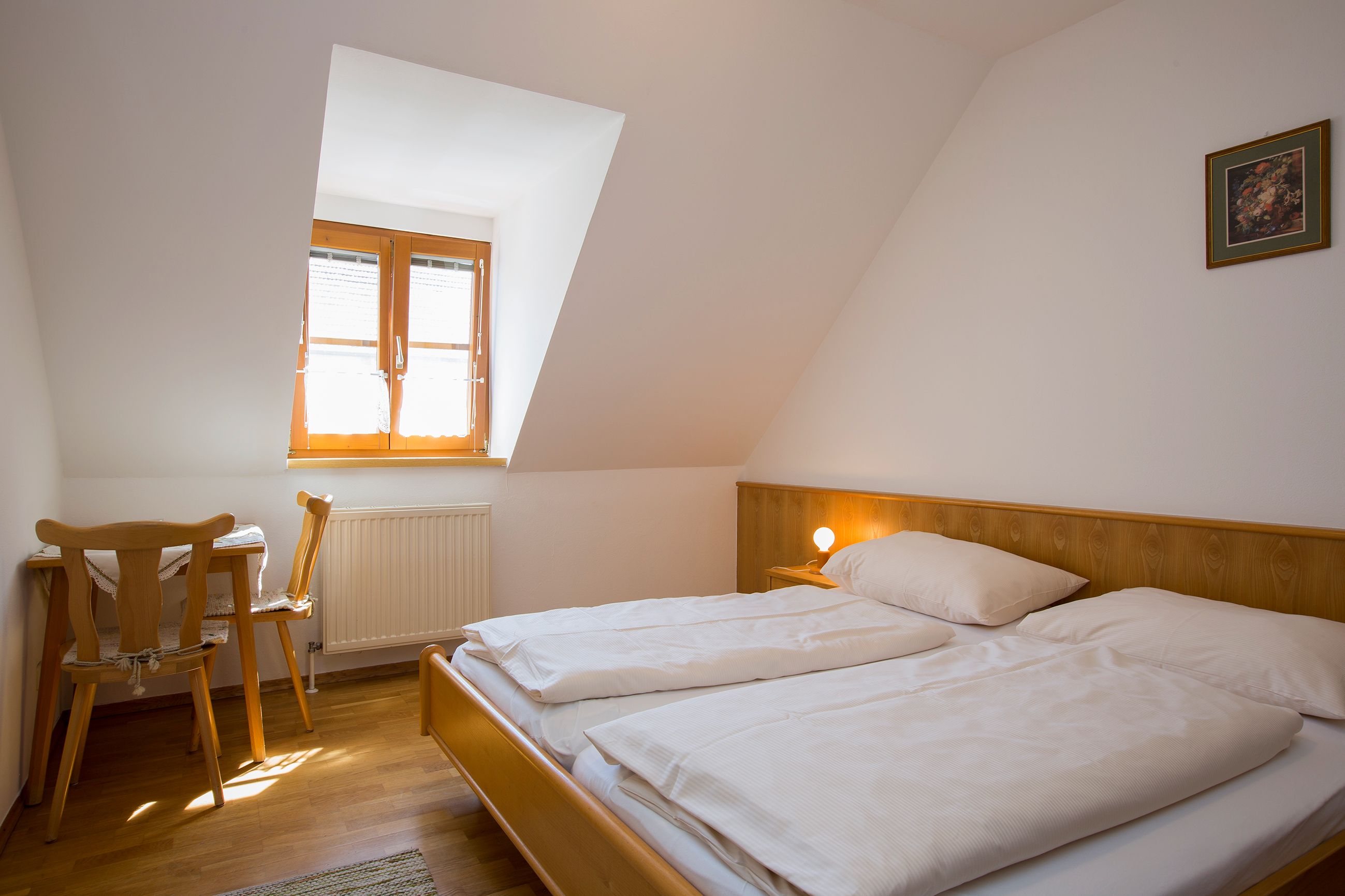 A simply furnished bedroom with a double bed, a small table and chair under a skylight.