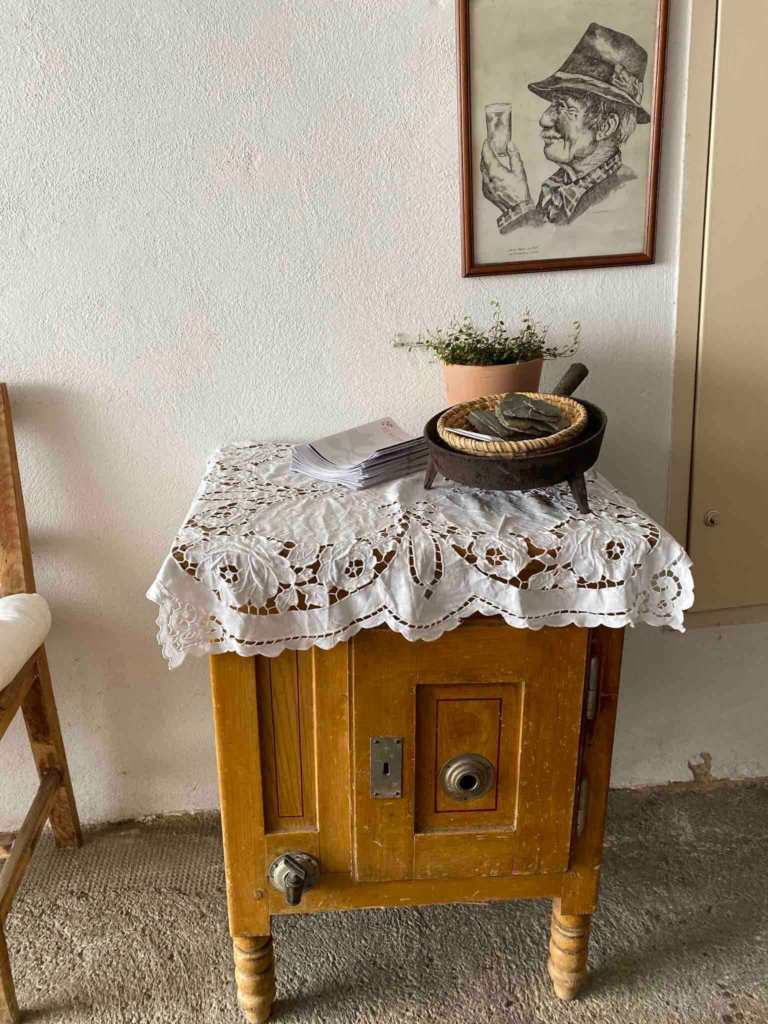 A small wooden table with a lace ceiling, plants and a framed picture on the wall.