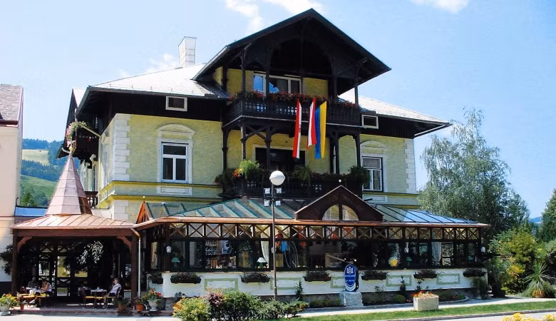 A traditional building with a glass veranda and Austrian flag, surrounded by plants.