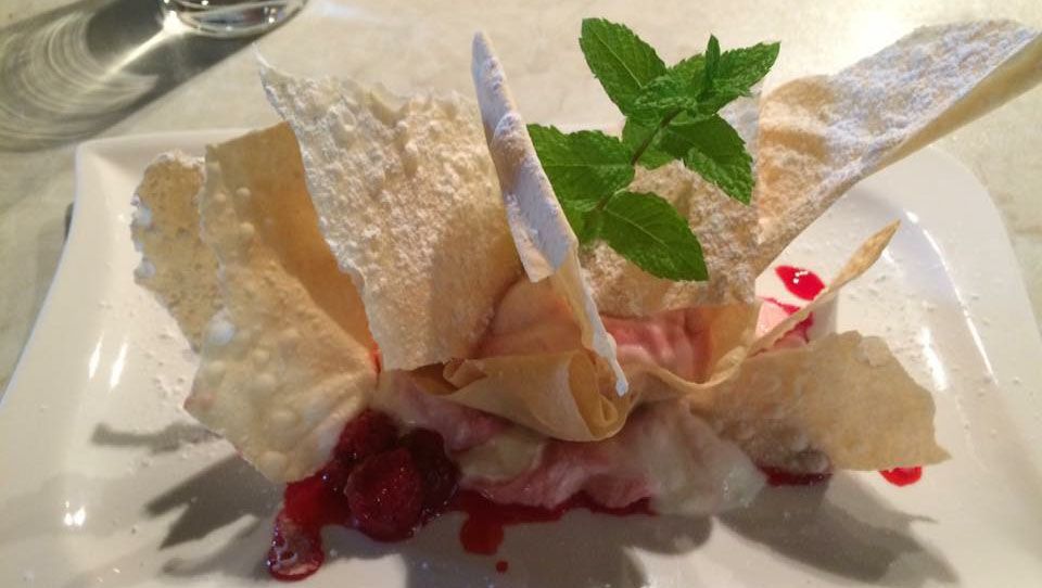 A dessert with raspberries, thin pastry sheets and mint on a white plate.