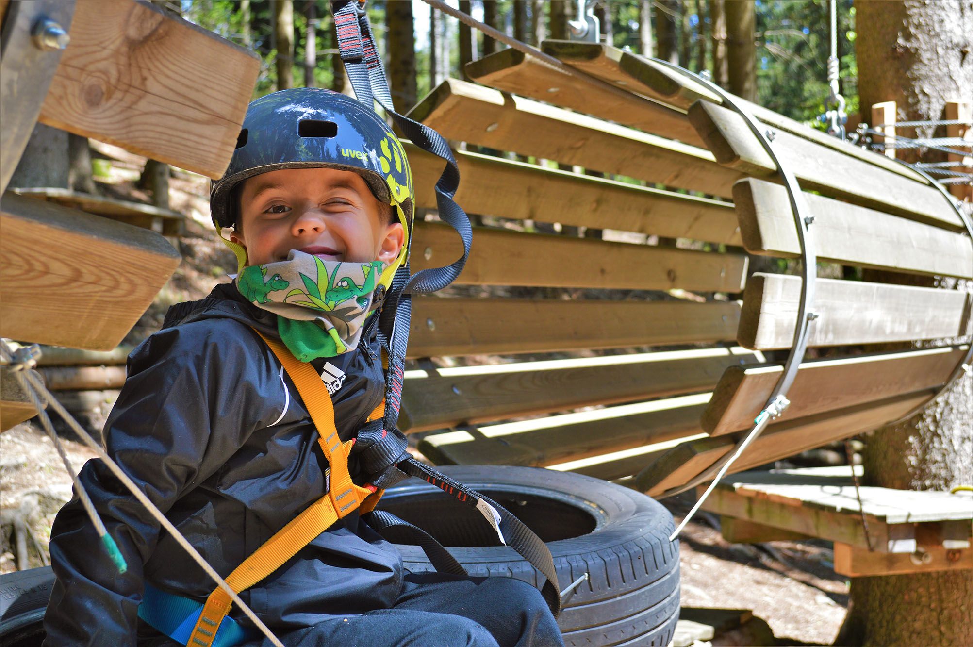A child wearing a helmet and safety harness in a climbing park.