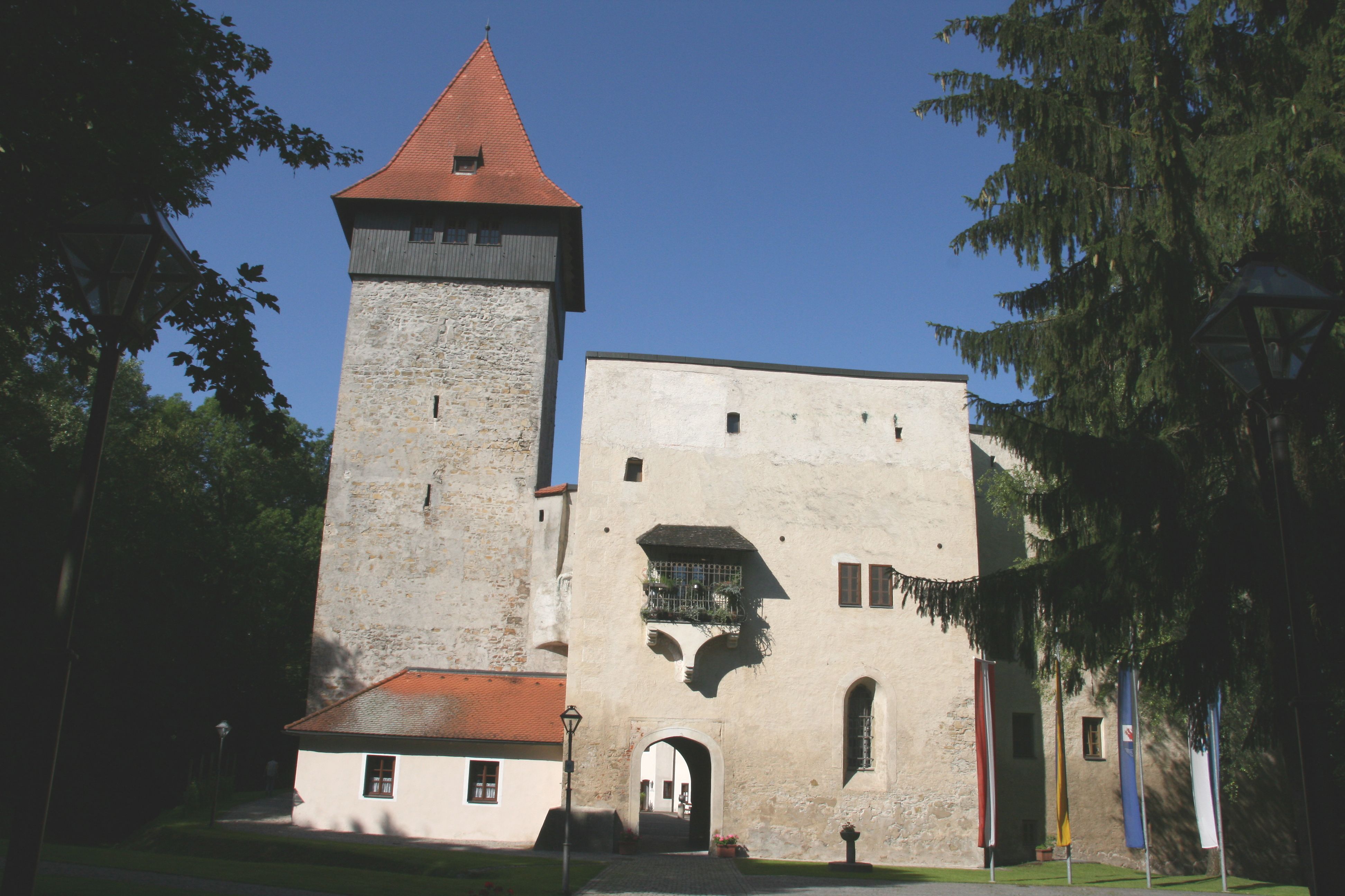 Ulmerfeld Castle with tower and entrance gate, surrounded by trees and flags.