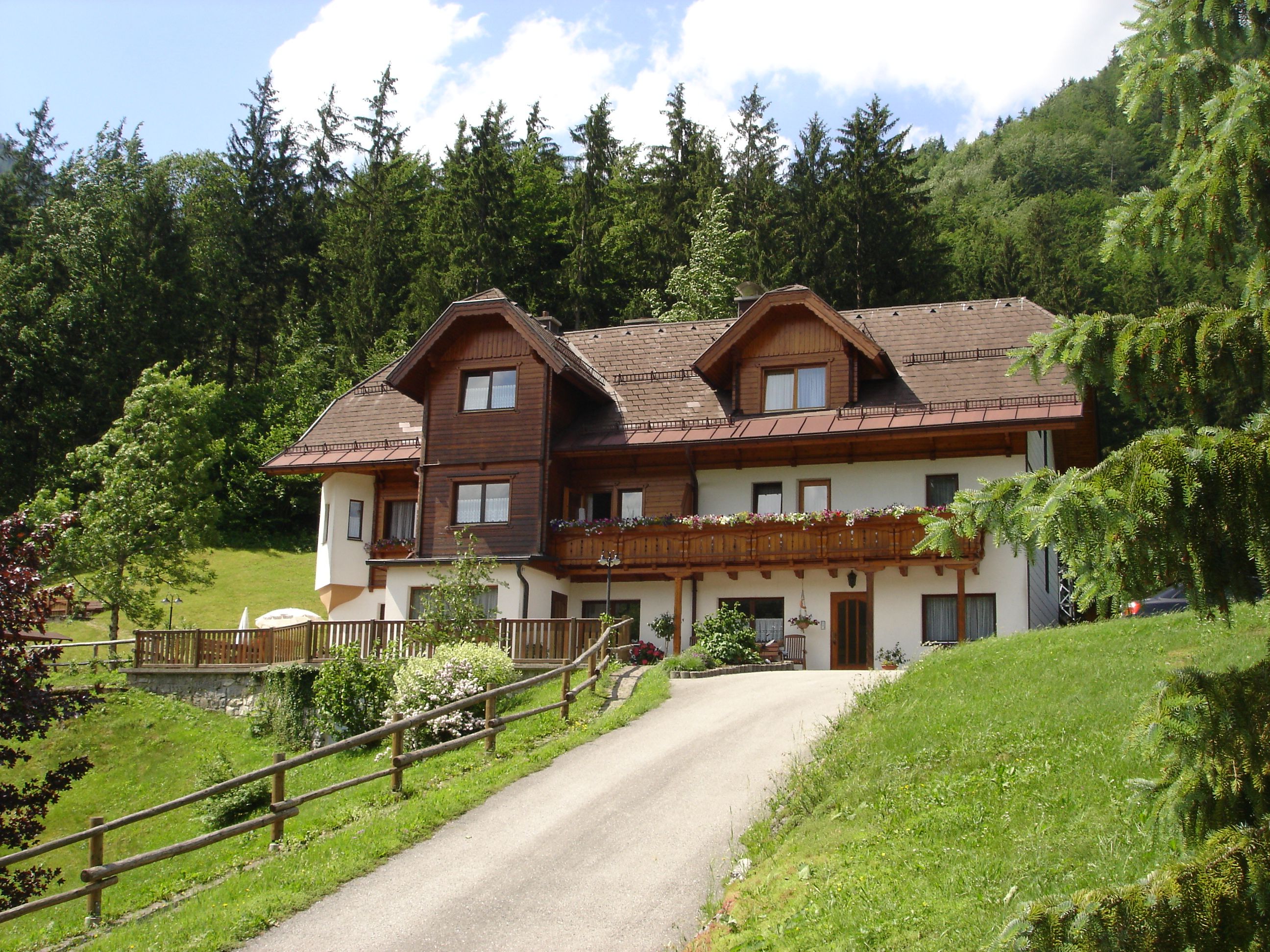 A traditional house with wooden cladding in a green, wooded setting.