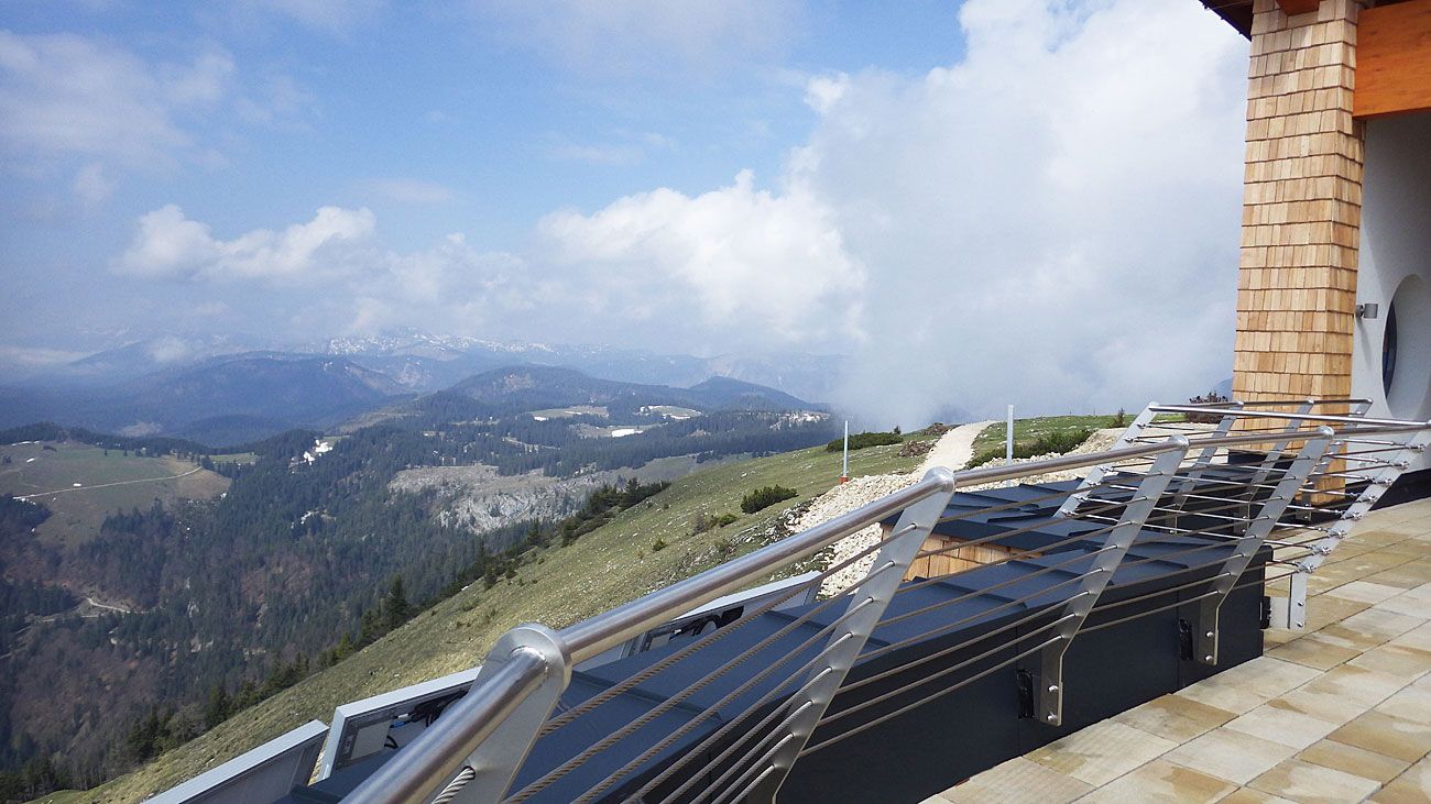 View from the Terzerhaus of a mountainous landscape with clouds and a railing in the foreground.